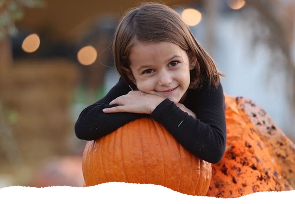 Smiling girl resting on a pumpkin at a Halloween pumpkin patch in London